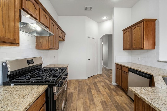 15205 Bullace St, Austin, TX 78724 - kitchen with appliances with stainless steel finishes, under cabinet range hood, arched walkways, dark wood-type flooring, and light stone counters
