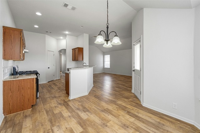 15205 Bullace St, Austin, TX 78724 - kitchen with gas range oven, arched walkways, brown cabinetry, vaulted ceiling, and a chandelier