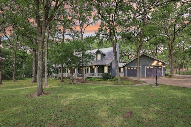 view of front of property with a lawn, a detached garage, covered porch, and metal roof