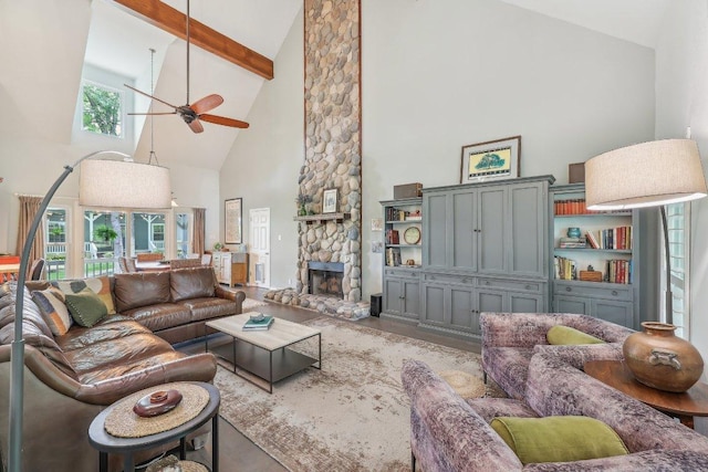 living room featuring beam ceiling, high vaulted ceiling, a stone fireplace, a ceiling fan, and wood finished floors