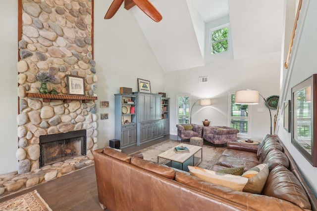 living area with high vaulted ceiling, a stone fireplace, wood finished floors, a healthy amount of sunlight, and visible vents