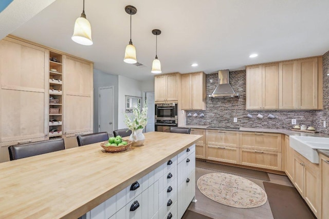 kitchen featuring light brown cabinetry, tasteful backsplash, a sink, butcher block counters, and wall chimney exhaust hood