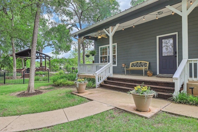 property entrance with a lawn, a ceiling fan, and fence
