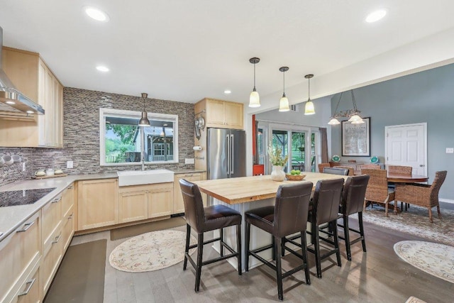 kitchen with light brown cabinetry, high end fridge, black electric stovetop, a sink, and backsplash