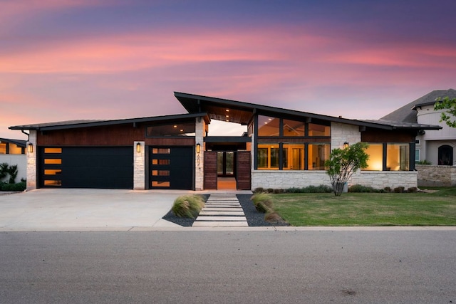 modern home with a yard, an attached garage, concrete driveway, and stone siding