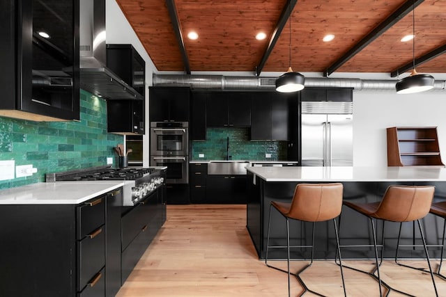 kitchen featuring a kitchen breakfast bar, appliances with stainless steel finishes, a sink, ventilation hood, and dark cabinets