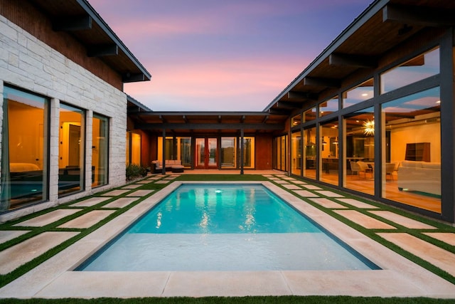 pool at dusk with french doors, a patio, and an outdoor pool