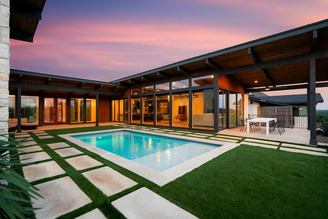 pool at dusk with a lawn, a patio, and an outdoor pool