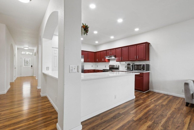 kitchen with appliances with stainless steel finishes, arched walkways, dark wood finished floors, dark brown cabinets, and under cabinet range hood
