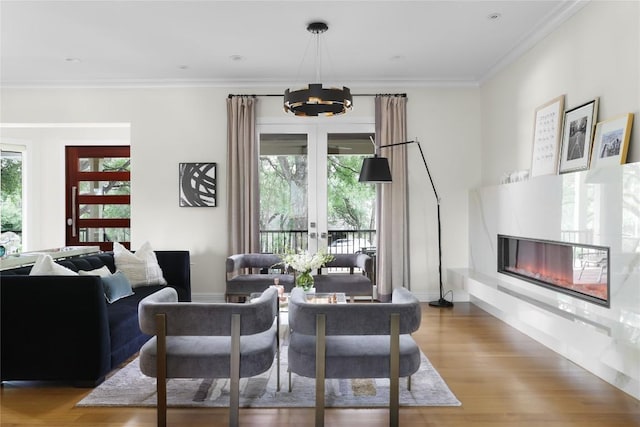 living area featuring crown molding, a glass covered fireplace, wood finished floors, and a notable chandelier