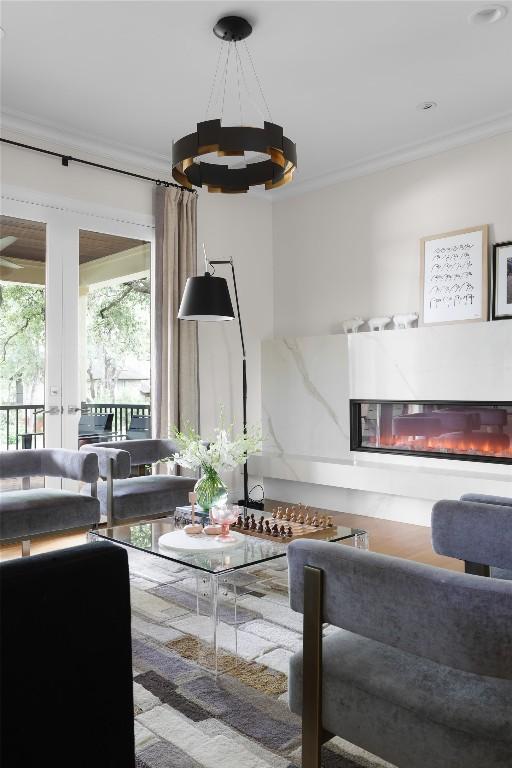 living area featuring a glass covered fireplace, ornamental molding, and a chandelier