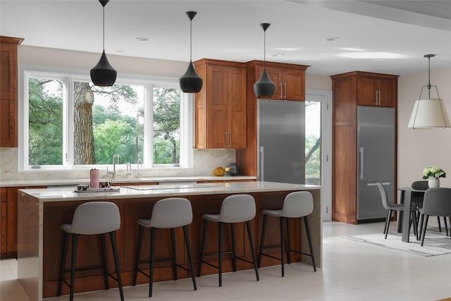 kitchen with a sink, built in refrigerator, tasteful backsplash, and pendant lighting