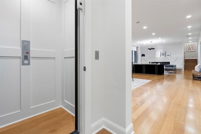 corridor featuring baseboards, recessed lighting, elevator, and light wood-style flooring