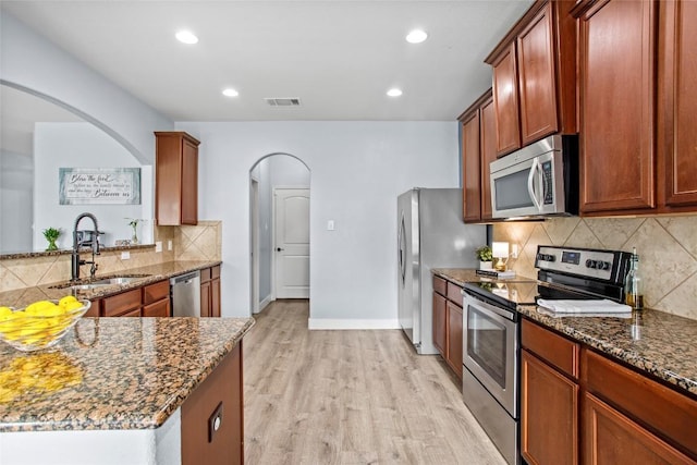 kitchen with a sink, light wood finished floors, arched walkways, stainless steel appliances, and visible vents