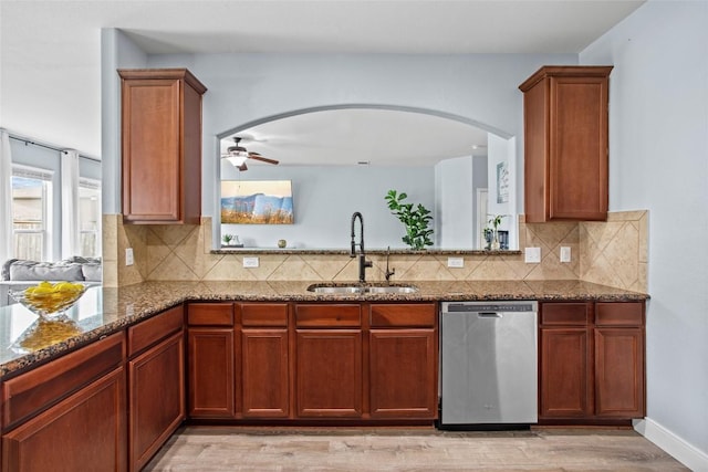 kitchen with a sink, dishwasher, arched walkways, dark stone countertops, and light wood-type flooring