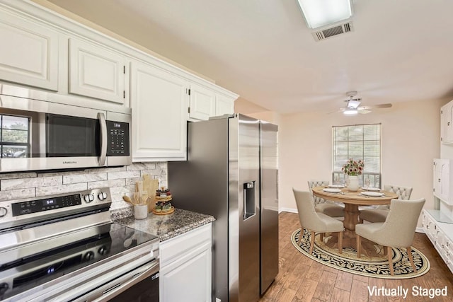 kitchen with ceiling fan, stainless steel appliances, white cabinetry, wood finished floors, and backsplash