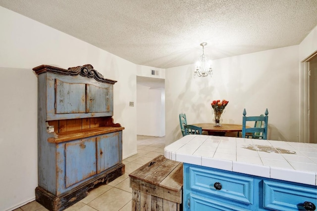interior space with blue cabinets, a textured ceiling, light tile patterned floors, an inviting chandelier, and tile counters