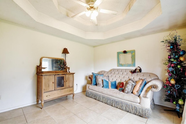 living area featuring baseboards, ceiling fan, light tile patterned floors, and a raised ceiling
