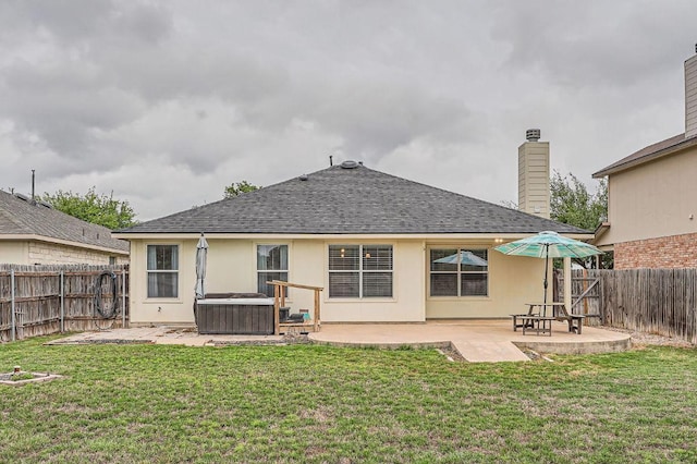 rear view of property with a fenced backyard, a hot tub, a patio area, and roof with shingles