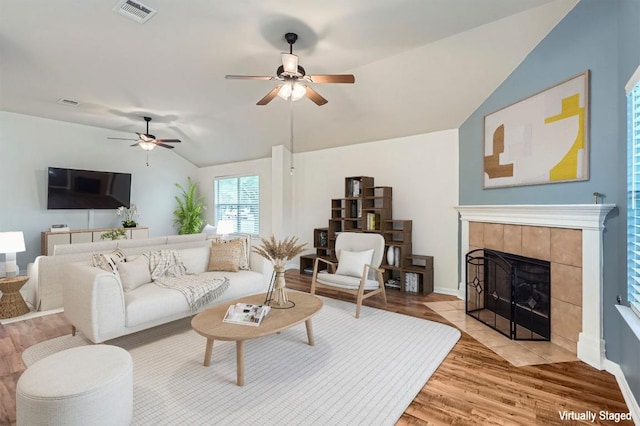 living area featuring a fireplace, a ceiling fan, lofted ceiling, light wood-type flooring, and visible vents