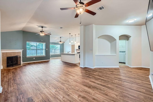 unfurnished living room featuring ceiling fan, washer / clothes dryer, a fireplace, wood finished floors, and baseboards