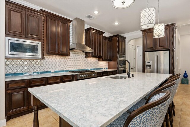 228 Cimarron Hills Trl E, Georgetown, TX 78628 - kitchen featuring stainless steel appliances, wall chimney exhaust hood, a breakfast bar, decorative light fixtures, and dark brown cabinets