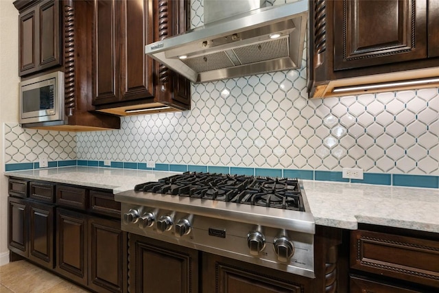 228 Cimarron Hills Trl E, Georgetown, TX 78628 - kitchen featuring wall chimney exhaust hood, appliances with stainless steel finishes, dark brown cabinets, decorative backsplash, and light stone counters