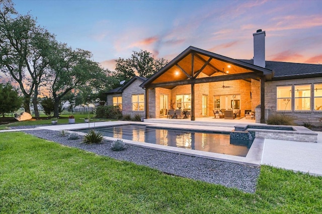 back of house at dusk with ceiling fan, an outdoor living space, a yard, a patio, and stone siding