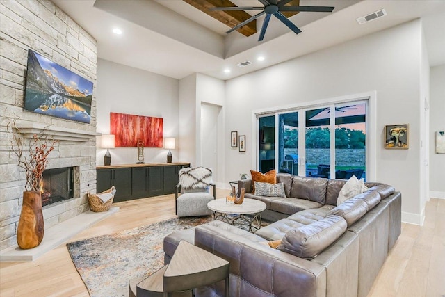 living room with ceiling fan, visible vents, a stone fireplace, and light wood-style floors