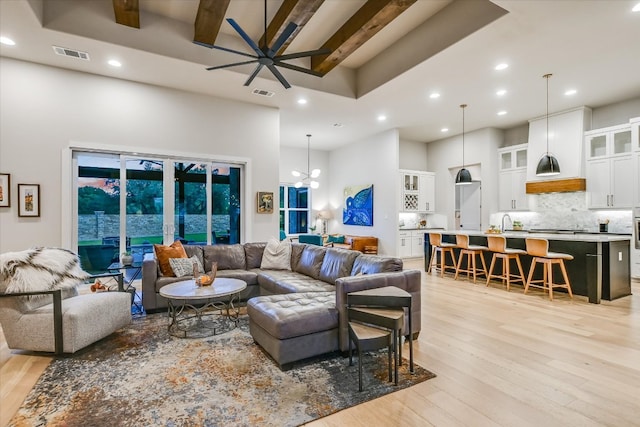 living room with visible vents, light wood finished floors, ceiling fan with notable chandelier, and a high ceiling