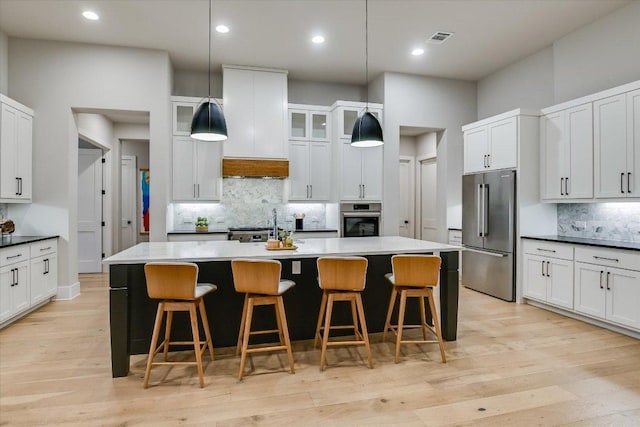 kitchen featuring visible vents, decorative backsplash, an island with sink, a breakfast bar area, and stainless steel appliances