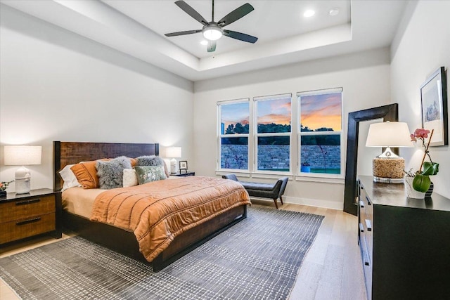 bedroom featuring ceiling fan, baseboards, light wood-style floors, a tray ceiling, and recessed lighting