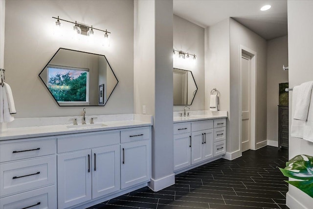 bathroom featuring baseboards, a sink, two vanities, and recessed lighting