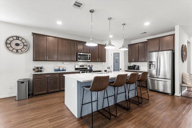 6401 Golden Bough Ln, Pflugerville, TX 78660 - kitchen with stainless steel appliances, dark brown cabinets, decorative backsplash, a kitchen island with sink, and dark wood finished floors
