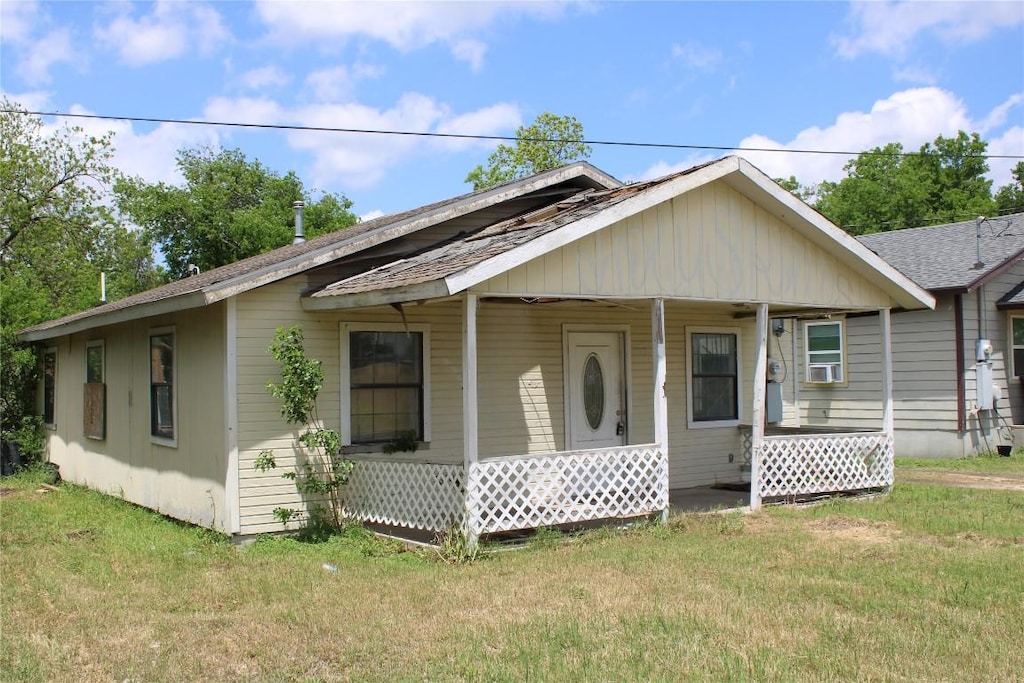bungalow with a shingled roof, cooling unit, a porch, and a front yard