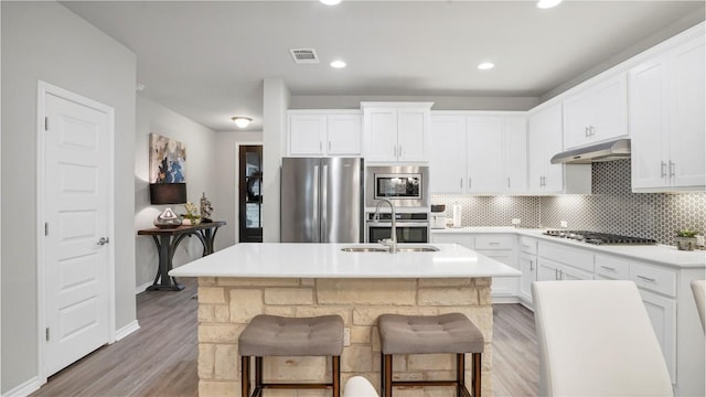 kitchen with light wood-style flooring, stainless steel appliances, decorative backsplash, under cabinet range hood, and visible vents