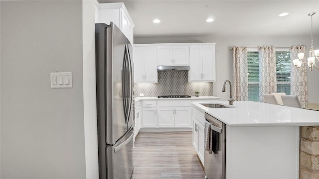 kitchen with under cabinet range hood, light countertops, a sink, a chandelier, and stainless steel appliances