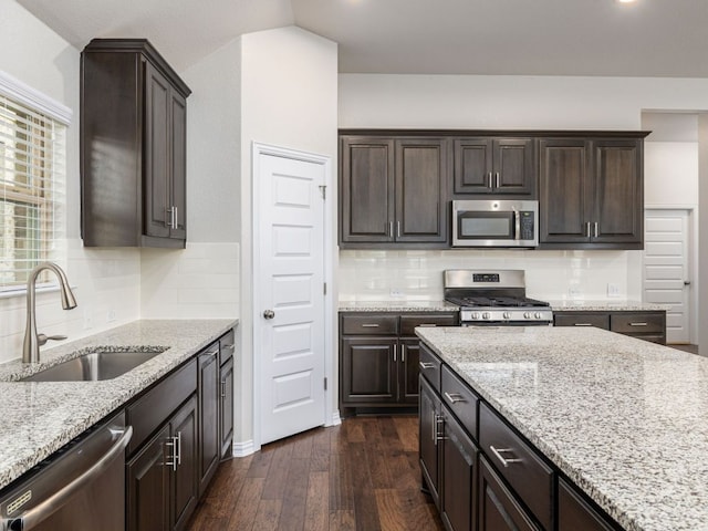 kitchen featuring dark brown cabinets, a sink, light stone counters, dark wood-style floors, and stainless steel appliances