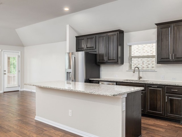 kitchen featuring a kitchen island, stainless steel refrigerator with ice dispenser, light stone countertops, vaulted ceiling, and a sink