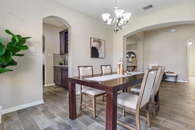 dining space featuring visible vents, arched walkways, wood finished floors, baseboards, and an inviting chandelier