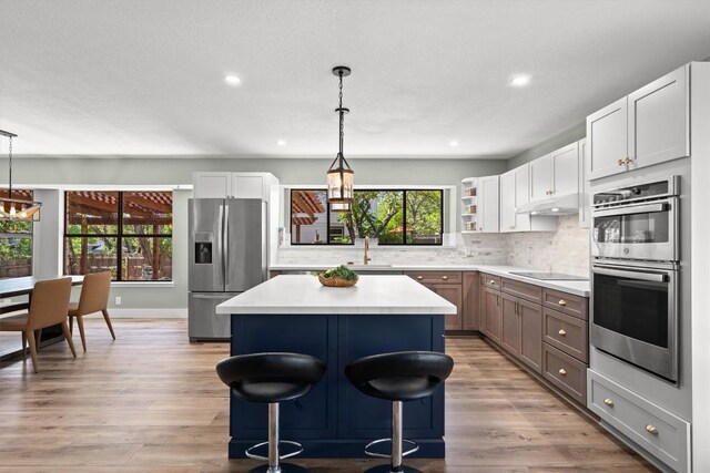 9800 Knotty Pine Cv, Austin, TX 78750 - kitchen featuring appliances with stainless steel finishes, under cabinet range hood, a kitchen island, open shelves, and light countertops