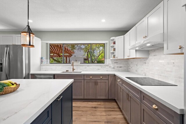 9800 Knotty Pine Cv, Austin, TX 78750 - kitchen featuring stainless steel fridge, black electric cooktop, under cabinet range hood, tasteful backsplash, and a sink
