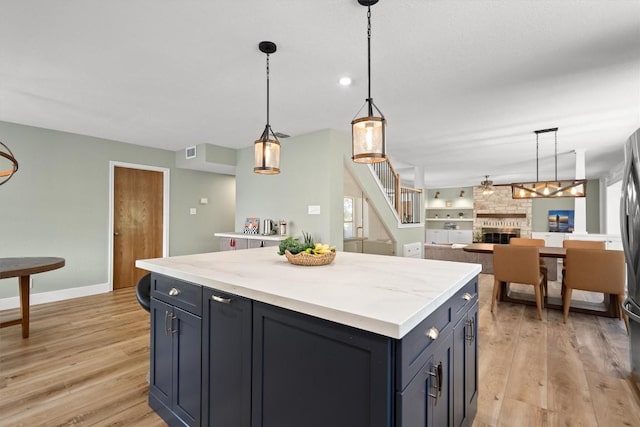 9800 Knotty Pine Cv, Austin, TX 78750 - kitchen featuring light wood-type flooring, a center island, pendant lighting, a stone fireplace, and open floor plan