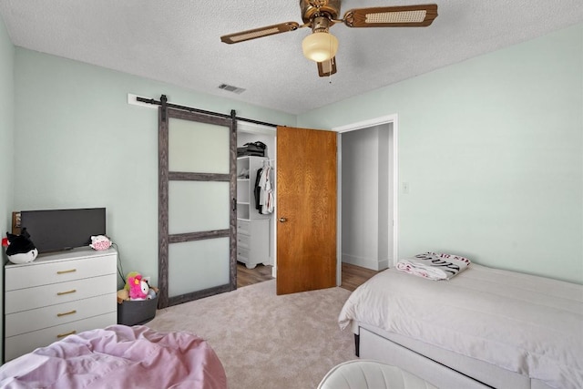 9800 Knotty Pine Cv, Austin, TX 78750 - carpeted bedroom featuring a barn door, a textured ceiling, and a ceiling fan