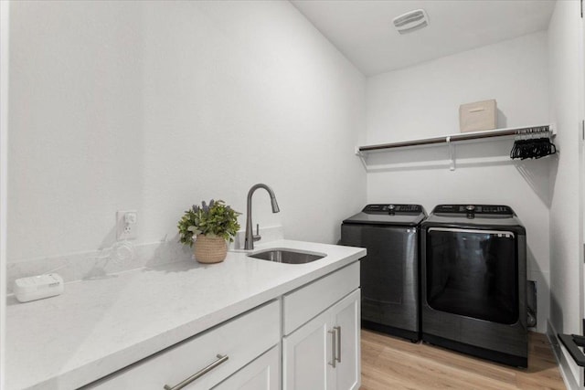 laundry area with cabinet space, a sink, light wood-style floors, visible vents, and washer and clothes dryer