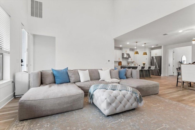 living area with recessed lighting, visible vents, light wood finished floors, and a towering ceiling