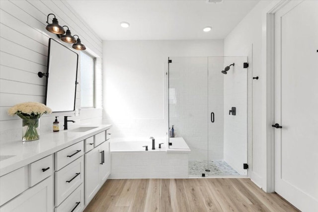 full bathroom featuring a sink, double vanity, wood finished floors, a garden tub, and a stall shower
