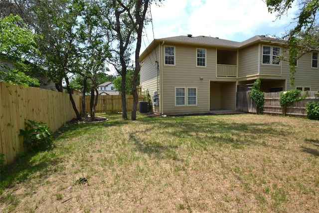 rear view of house with a fenced backyard, a balcony, a yard, and central AC unit