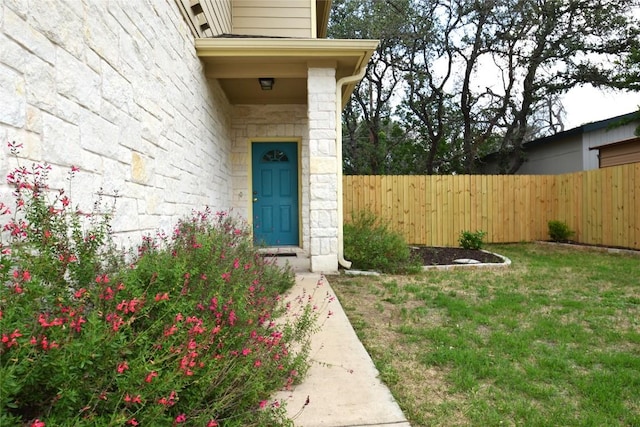 entrance to property featuring fence, a yard, and stone siding