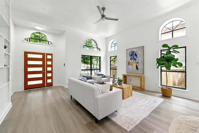 7419 Dallas Dr, Austin, TX 78729 - living room featuring a textured ceiling, light wood finished floors, a ceiling fan, baseboards, and a towering ceiling